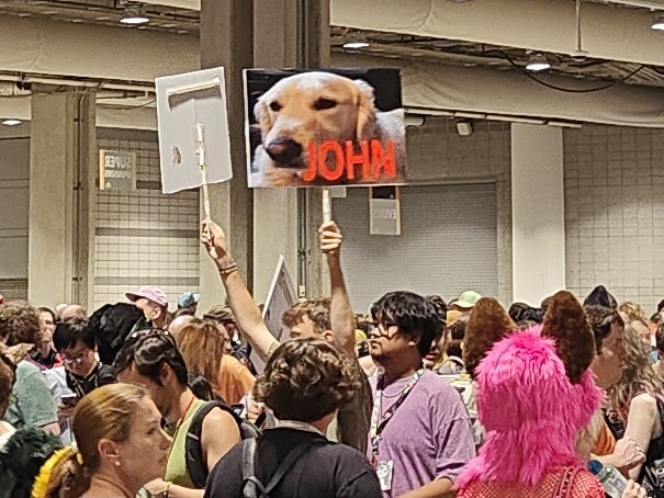 Someone holding up a sign of a golden retriever captioned "JOHN" in a red
sans-serif font