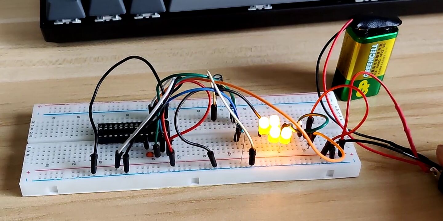 
    Breadboard on which an NE555P and four illuminating yellow LEDs are
    seen. A 9V battery is behind, powering the circuit

