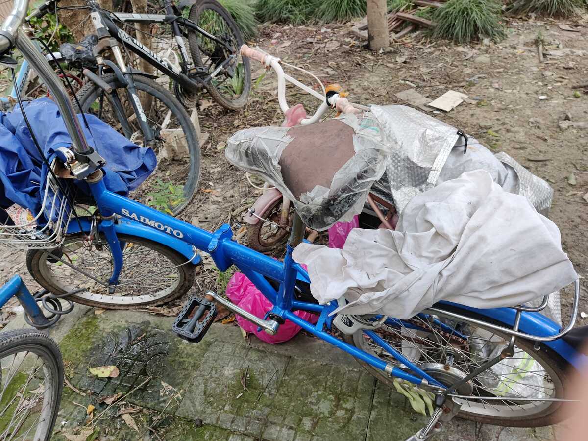 A blue bike covered with a raincoat and pieces of rag