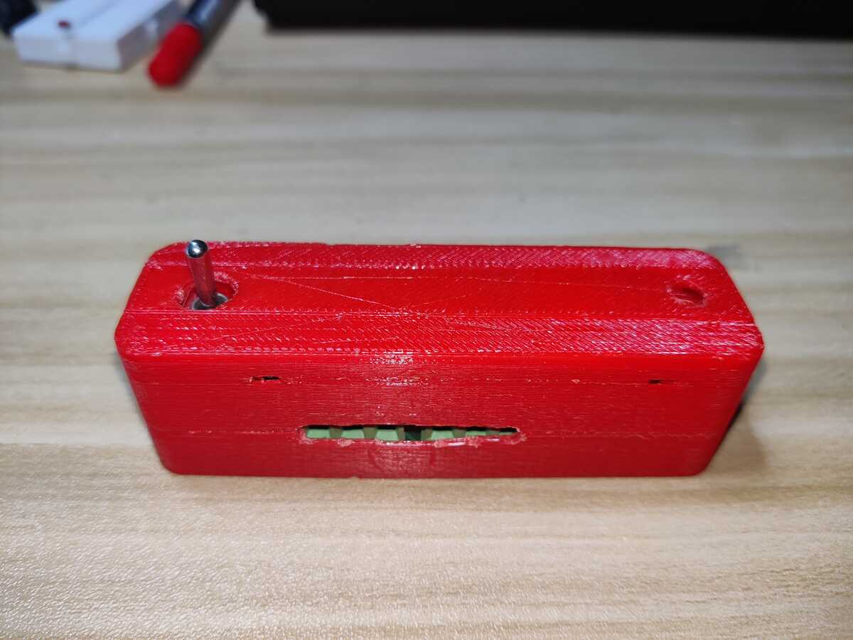 
        Front view of the case. A toggle switch extrudes through a hole on
        its top left. On the front there is a wide slit, behind which you
        can see part of the screw terminals.
    