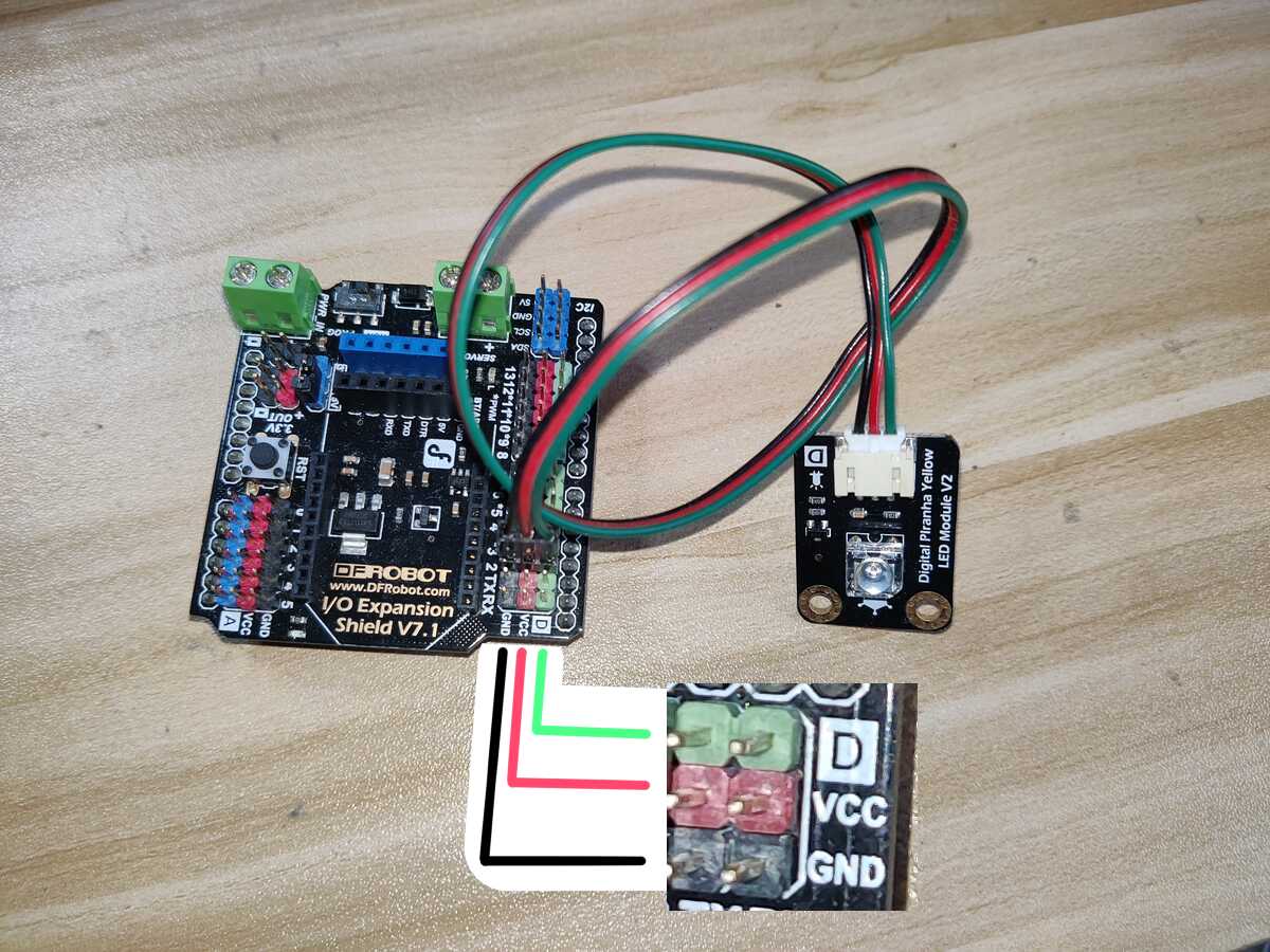 A DFRobot "I/O Expansion Shield V7.1" for Arduino Uno. There is a rail
of pin headers in three rows: GND, VCC and D. An LED module from the same
kit is connected via three jumper wires.