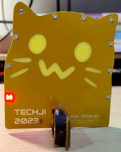Yellow PCB standing, colorful LEDs in marquee mode. Printed on PCB:
"TechJI 2023" and "owo :blobcat:"