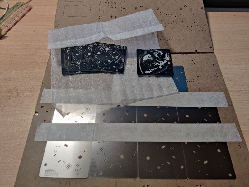 Shiny stencils taped on cardboard, with black PCBs placed on
top