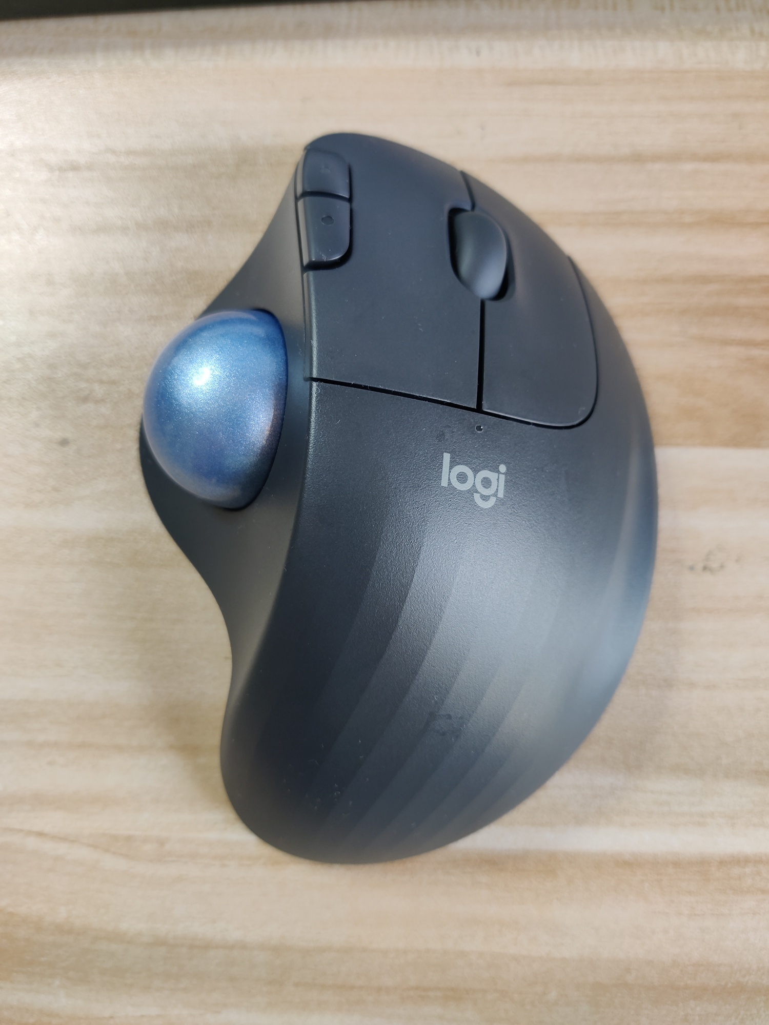 Top view of the trackball. It is asymmetric. A shiny blue trackball (3-4
cm in diameter) is on the left. The chassis on the right is made of black
plastic, has a "logi" logo, and features two mouse buttons and
a scrollwheel. At the tip of the left button there are two protruding
buttons in a vertical layout.